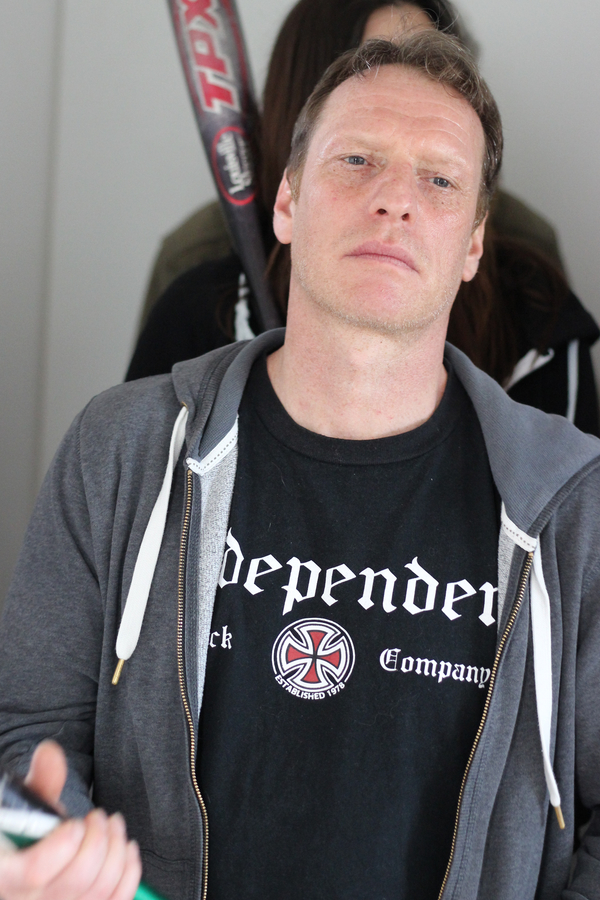 Mann in grauem Hoodie und schwarzem T-Shirt mit dem Schriftzug 'Independent', hält einen Baseballschläger.