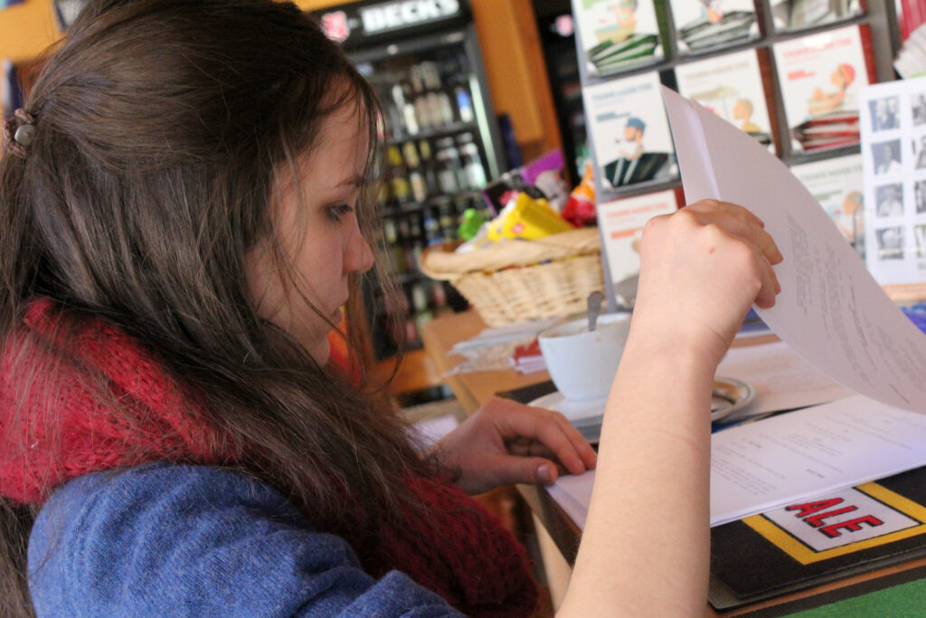 Junge Frau mit langen Haaren, die eine Speisekarte in einem Café studiert, während sie an einem Tisch sitzt.